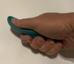 A green, thumb-shaped plastic massage tool designed for deep tissue and trigger point therapy, held in a hand.