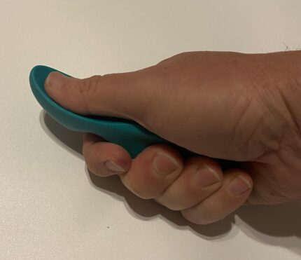 A green, thumb-shaped plastic massage tool designed for deep tissue and trigger point therapy, held in a hand.
