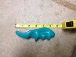 A green, thumb-shaped plastic massage tool designed for deep tissue and trigger point therapy, held in a hand.
