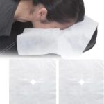 Stack of 100 white UtySty disposable face cradle covers on a massage table headrest.