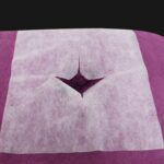 Stack of 100 white UtySty disposable face cradle covers on a massage table headrest.