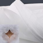 Stack of 100 white UtySty disposable face cradle covers on a massage table headrest.