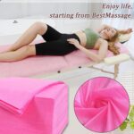 Stack of 100 individually folded pink disposable massage table sheets, made of non-woven fabric, ready for use.